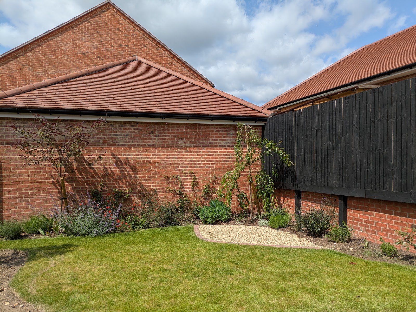 A tricky new-build corner softened with a gravel-set bed of grasses and perennials against the brick and dark cladding.